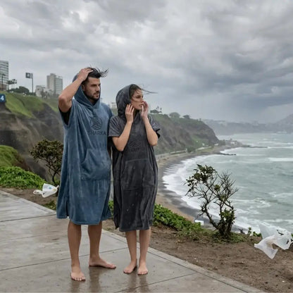 Pareja de nadadores usando ponchos cambiadores Sharka de 400 gsm frente al mar en la Costa Verde Lima